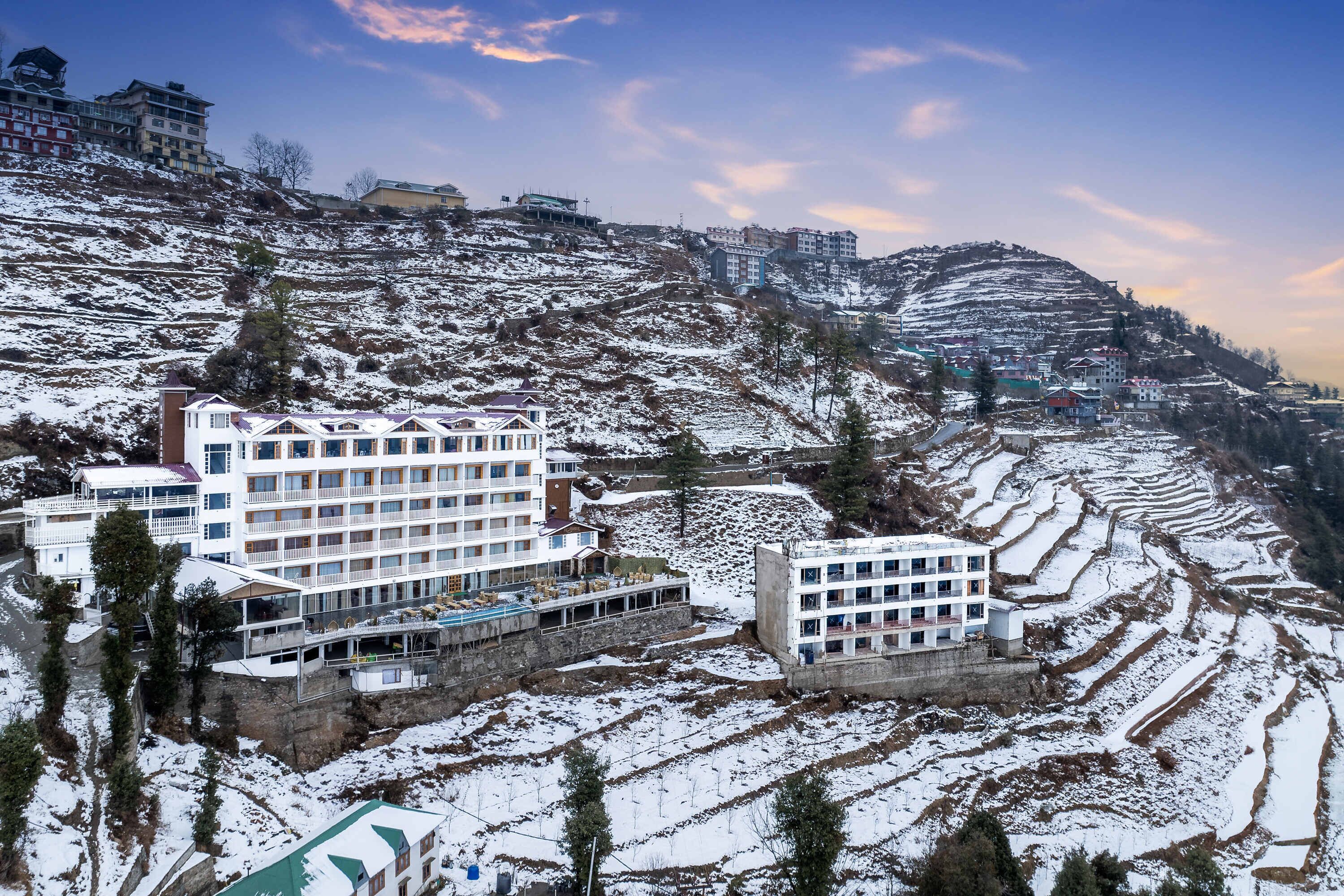 A hotel with multiple floors, terraced rice fields, and a mountainous backdrop.