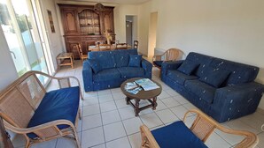 Un amplio espacio de sala con un sofá azul, sillas de mimbre y una mesa de comedor.