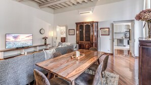 A modern living room with a wooden dining table, grey upholstered seating, a large flat-screen TV, and a kitchen in the background. - Spacious Apt in the Center of Rome  (Roma)