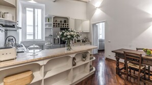 A modern kitchen with white cabinetry, a wooden dining table, and a vase of flowers on the counter. - Spacious Apt in the Center of Rome  (Roma)