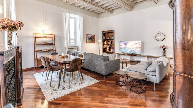 A spacious living room with a wooden floor, a grey sofa, a dining table with chairs, and a bookshelf. - Spacious Apt in the Center of Rome  (Roma)