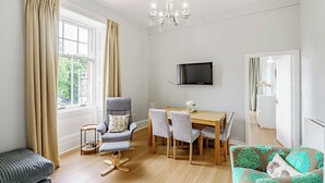 A modern living room with a dining area, a sofa, a TV mounted on the wall, and a window with curtains. - Spacious City Apartment - Dunfermline (Dunfermline)