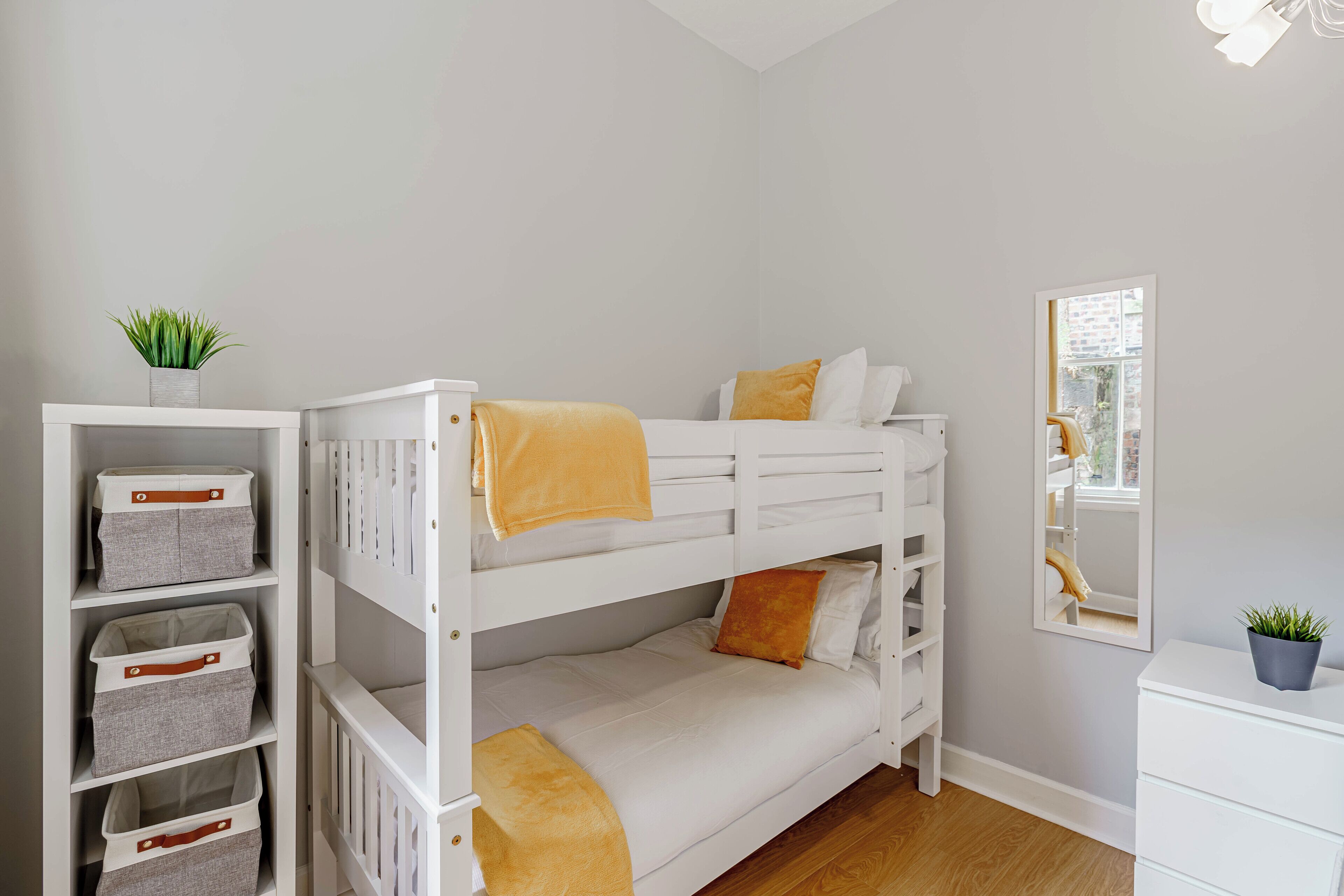 A bunk bed with storage drawers, a mirror, and a potted plant.