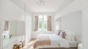 A bedroom with a bed, a vanity with a mirror, and a window with curtains. - Spacious City Apartment - Dunfermline (Dunfermline)
