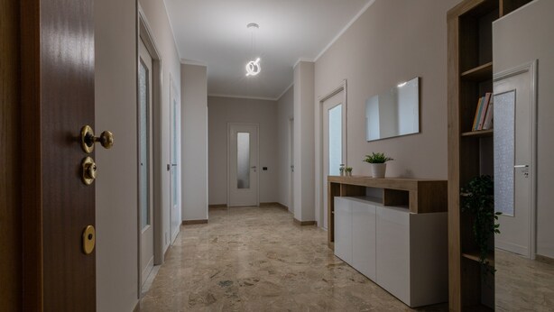 A hallway with a marble floor, wooden doors, a white console table with a plant, and a mirror on the wall. - Torino Modern Stay by Wonderful Italy (Turin)