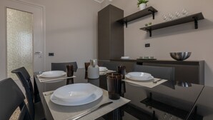 A modern dining area with a glass table, black chairs, and a kitchen in the background. - Torino Modern Stay by Wonderful Italy (Turin)