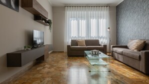 A modern living room with a flat-screen TV, two sofas, a glass coffee table, and a large window with sheer curtains. - Torino Modern Stay by Wonderful Italy (Turin)