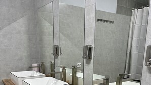A modern bathroom with three white sinks, wooden vanity, and large mirrors.