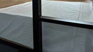 A room with a wooden ceiling and walls, a bed with white bedding, and a wall-mounted light fixture.
