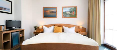 Habitación de hotel con una cama grande, televisión, escritorio y dos cuadros en la pared.