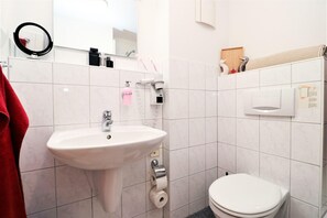 Ett badrum med ett vitt handfat, en toalett och en spegel med en ringformad lampa.