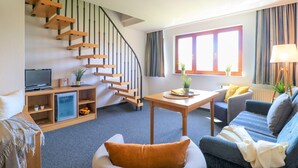 A living room with a wooden staircase, a television, a table with a plant, and a sofa.