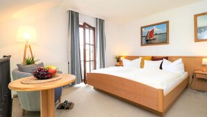 Une chambre d’hôtel avec un grand lit, une table de chevet avec une lampe, un panier de fruits, une chaise et une vue sur l’extérieur par une fenêtre.