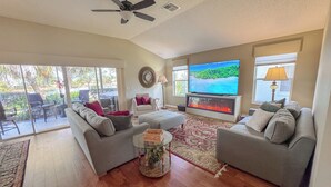 Ein Wohnzimmer mit zwei grauen Sofas, einem Couchtisch, einem Flachbildfernseher, einem Kamin und einem Deckenventilator.