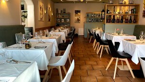 A restaurant with multiple tables set for dining, a wine rack on the wall, and a ceiling light fixture. - Sterne Luxus Heidesonne (Jesteburg)