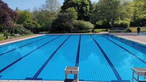A clear blue swimming pool with lane dividers, surrounded by lush greenery and trees. - Sterne Luxus Heidesonne (Jesteburg)
