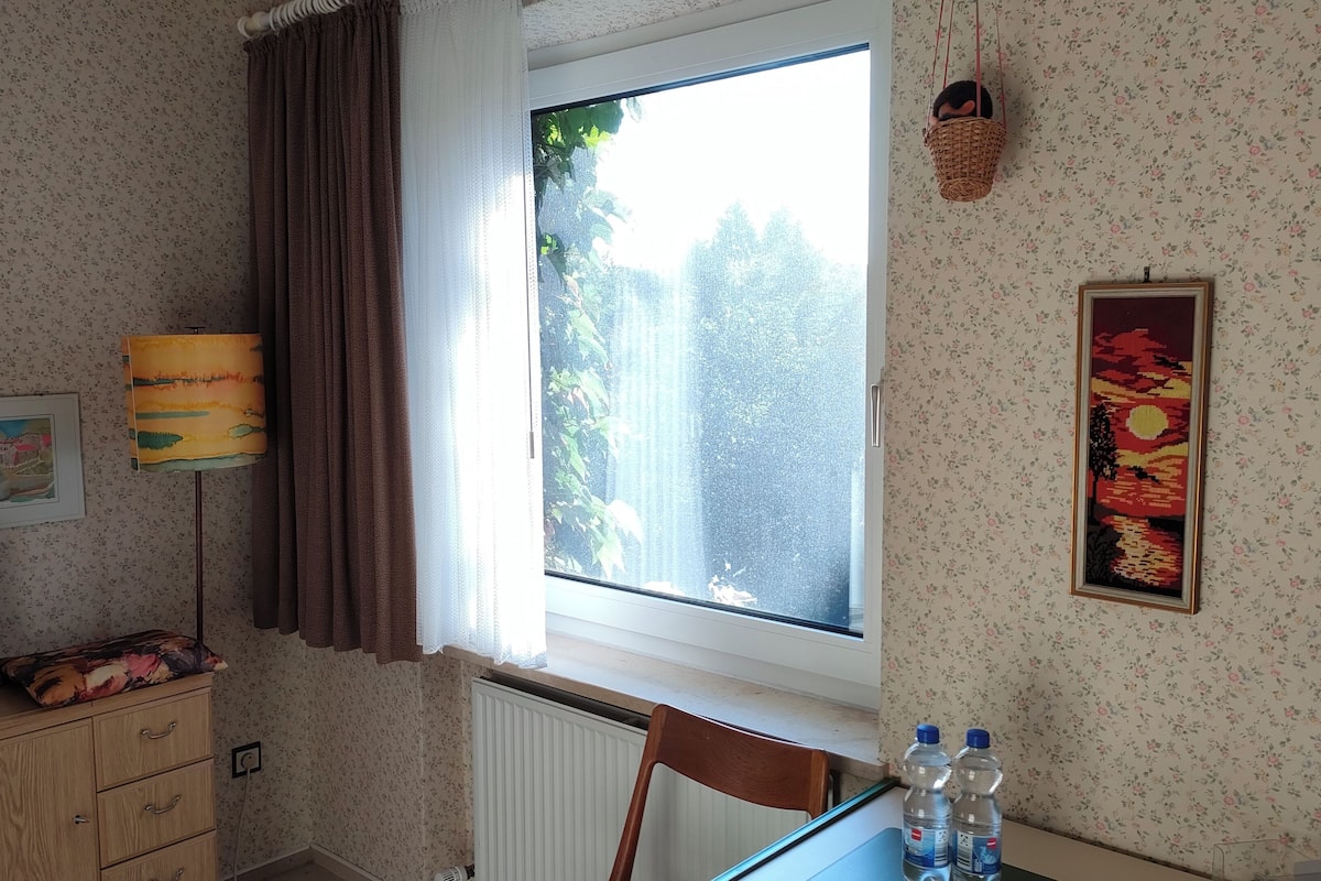 A room with a window, a radiator, a wooden dresser, a chair, and two water bottles on a table.