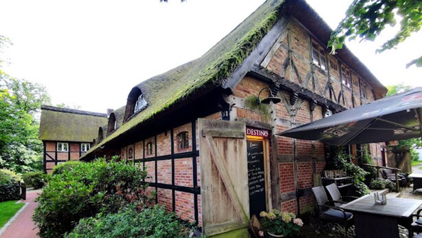 A traditional half-timbered building with a thatched roof, a sign reading "DESTINO," and outdoor seating with umbrellas. - Sterne Luxus Heidesonne (Jesteburg)