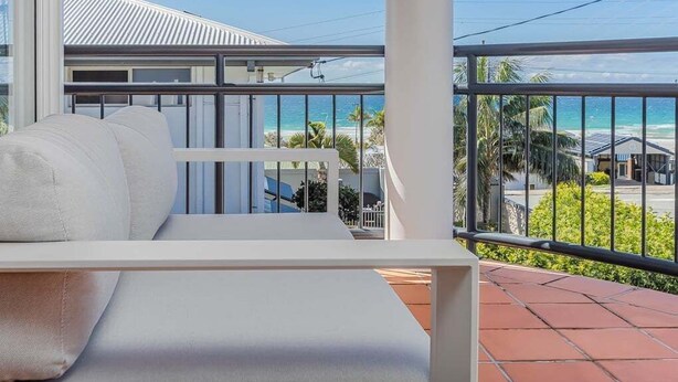 A balcony with a white sofa, a view of the beach, and a clear sky.