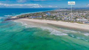 An aerial view of a coastal area with clear turquoise waters, a sandy beach, and a residential area with buildings.