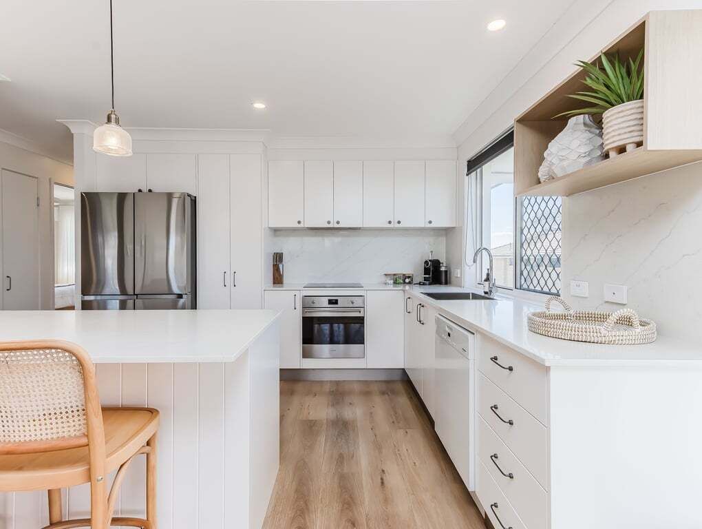 Una cocina moderna con armarios blancos, un refrigerador de acero inoxidable, un horno y un comedor con una silla de madera.