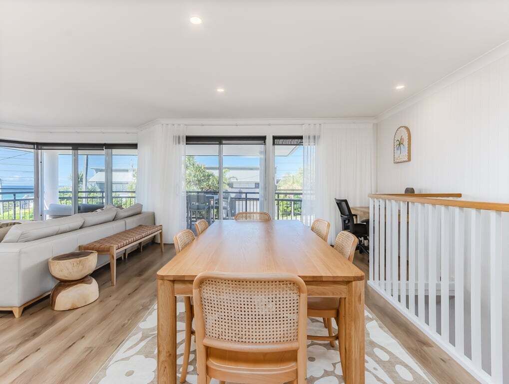 Amplia habitación con una gran mesa de comedor de madera, paredes blancas y un balcón con vista al mar.