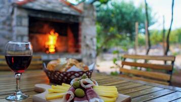 A wooden table with a glass of red wine, a wooden cutting board with cheese, olives, and prosciutto, and a basket of bread.