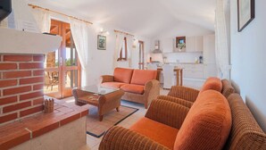 A cozy living room with a brick fireplace, wicker furniture, and a kitchen in the background. - Holiday Home Stomorica (Sutivan)
