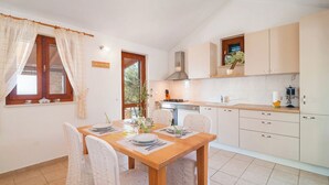 A modern kitchen with a dining table set for four, wooden cabinets, and a window with curtains. - Holiday Home Stomorica (Sutivan)
