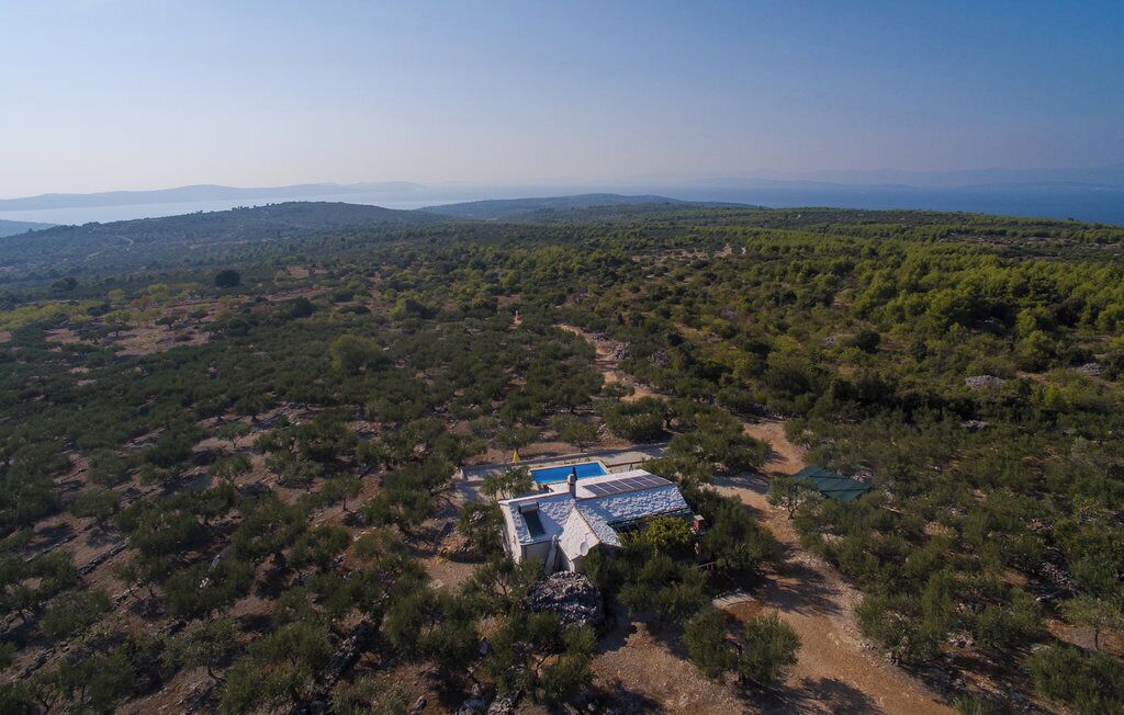 An aerial view of a property with a swimming pool, surrounded by dense vegetation and hills in the background.