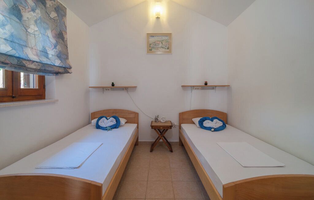 A small, clean room with two single beds, a small table, and a window with a curtain.