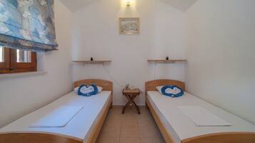 A small, clean room with two single beds, a small table, and a window with a curtain.