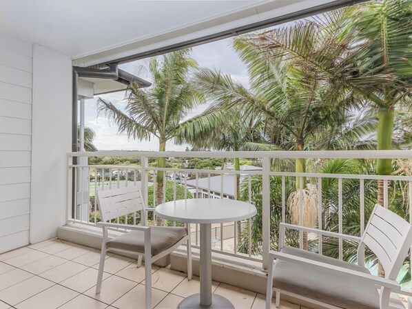 Een balkon met een witte reling, een ronde tafel en twee stoelen.