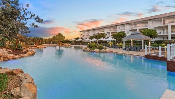 Un hotel con piscina, mobiliario exterior y un edificio de varios pisos.