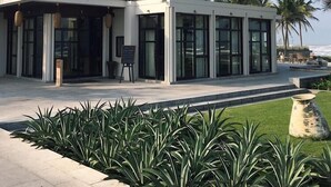 Un edificio moderno con amplios ventanales, un acceso cubierto y un césped cuidado con plantas tropicales.
