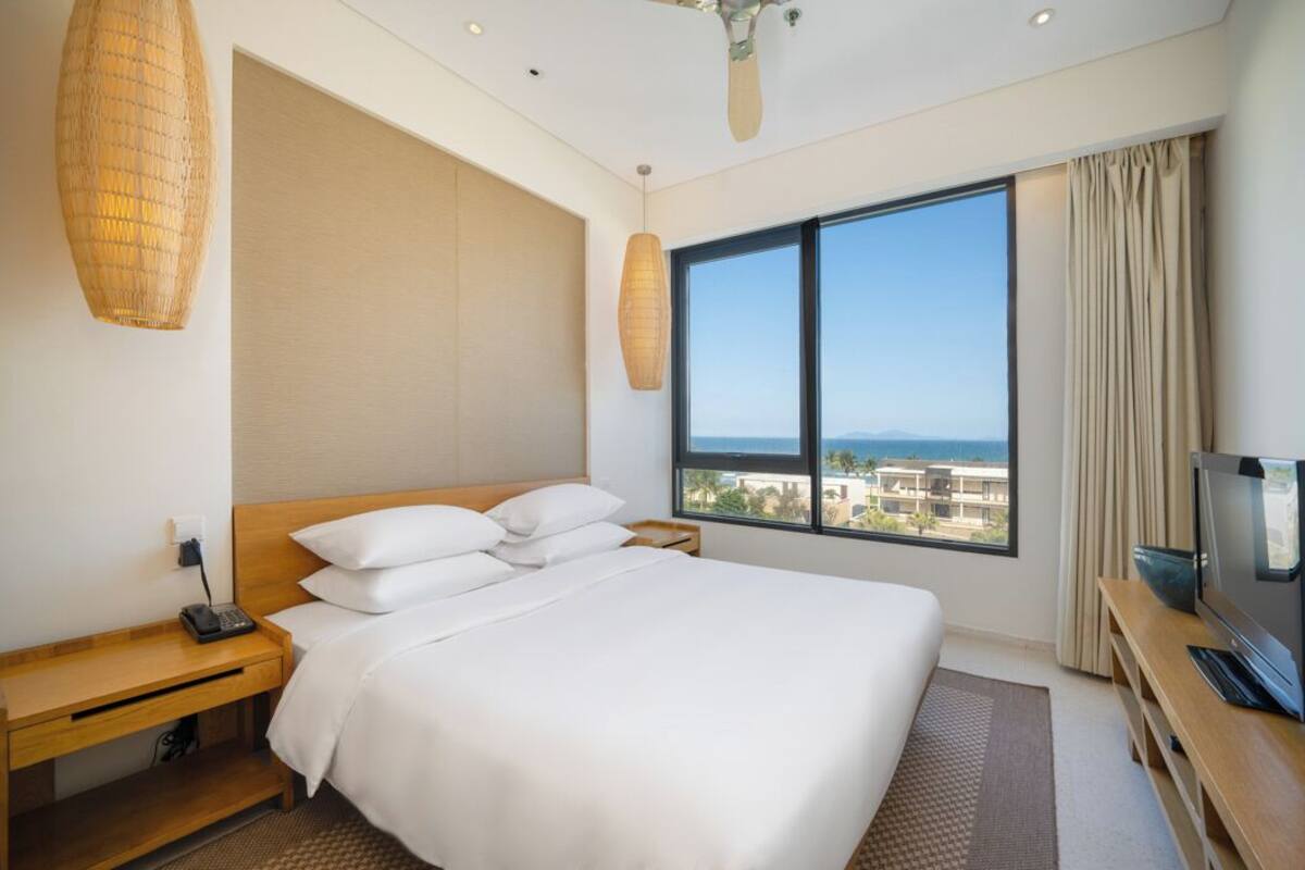 Une chambre d’hôtel avec un grand lit, une télévision, un bureau avec un téléphone et une fenêtre donnant sur la ville.