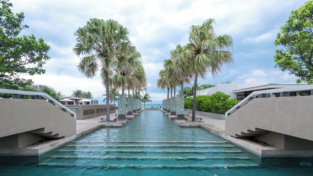 Una piscina con vista despejada del agua, rodeada de palmeras y arquitectura moderna.