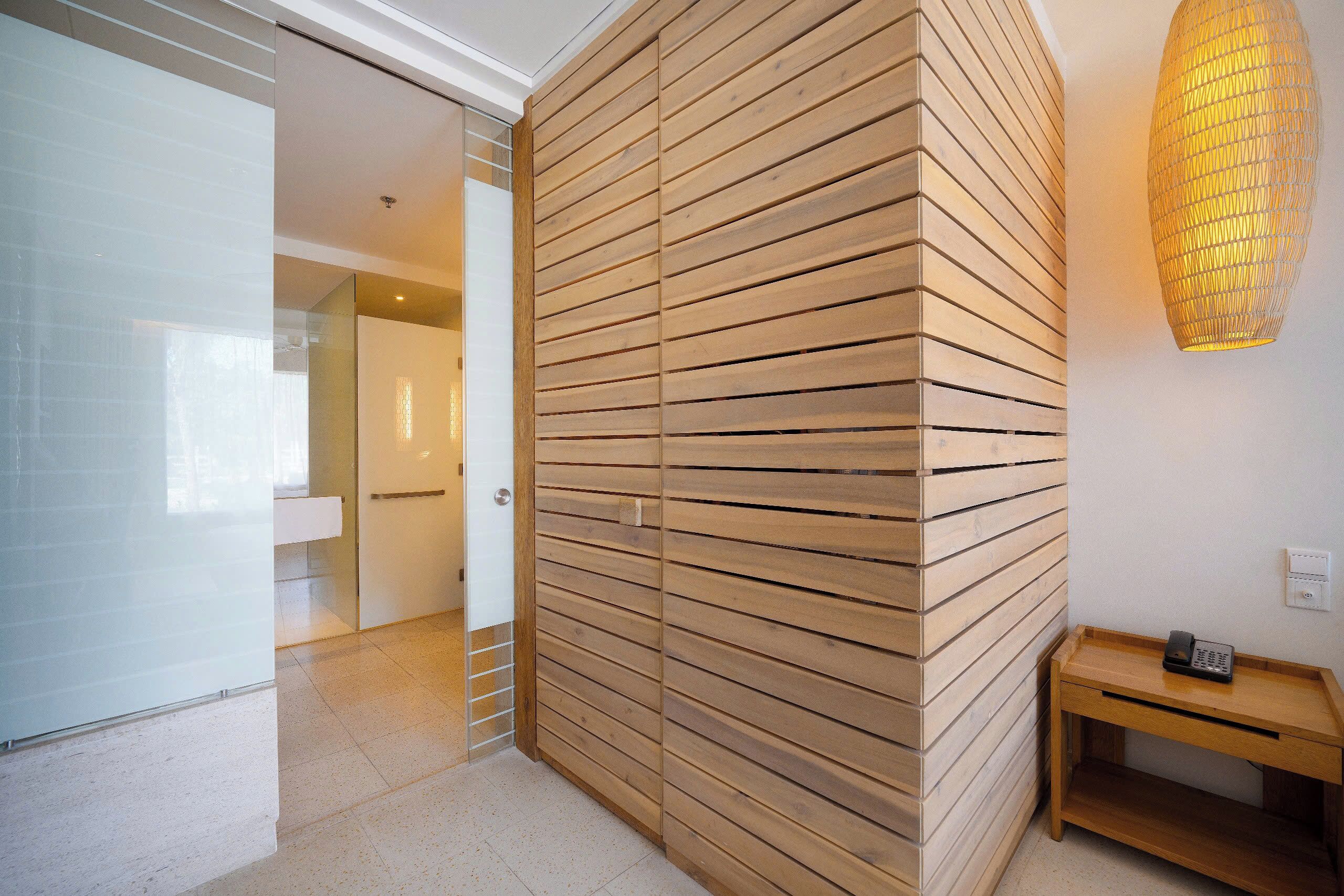 Un interior moderno con un panel de madera en la pared, una puerta de cristal que da a otra habitación, y una pequeña mesa de madera con un teléfono.