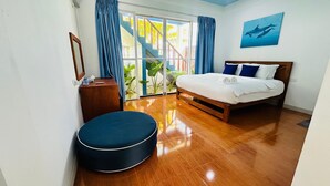 Un dormitorio con una cama de madera, un otoman redondo, un pequeño aparador de madera y un ventanal con cortinas.