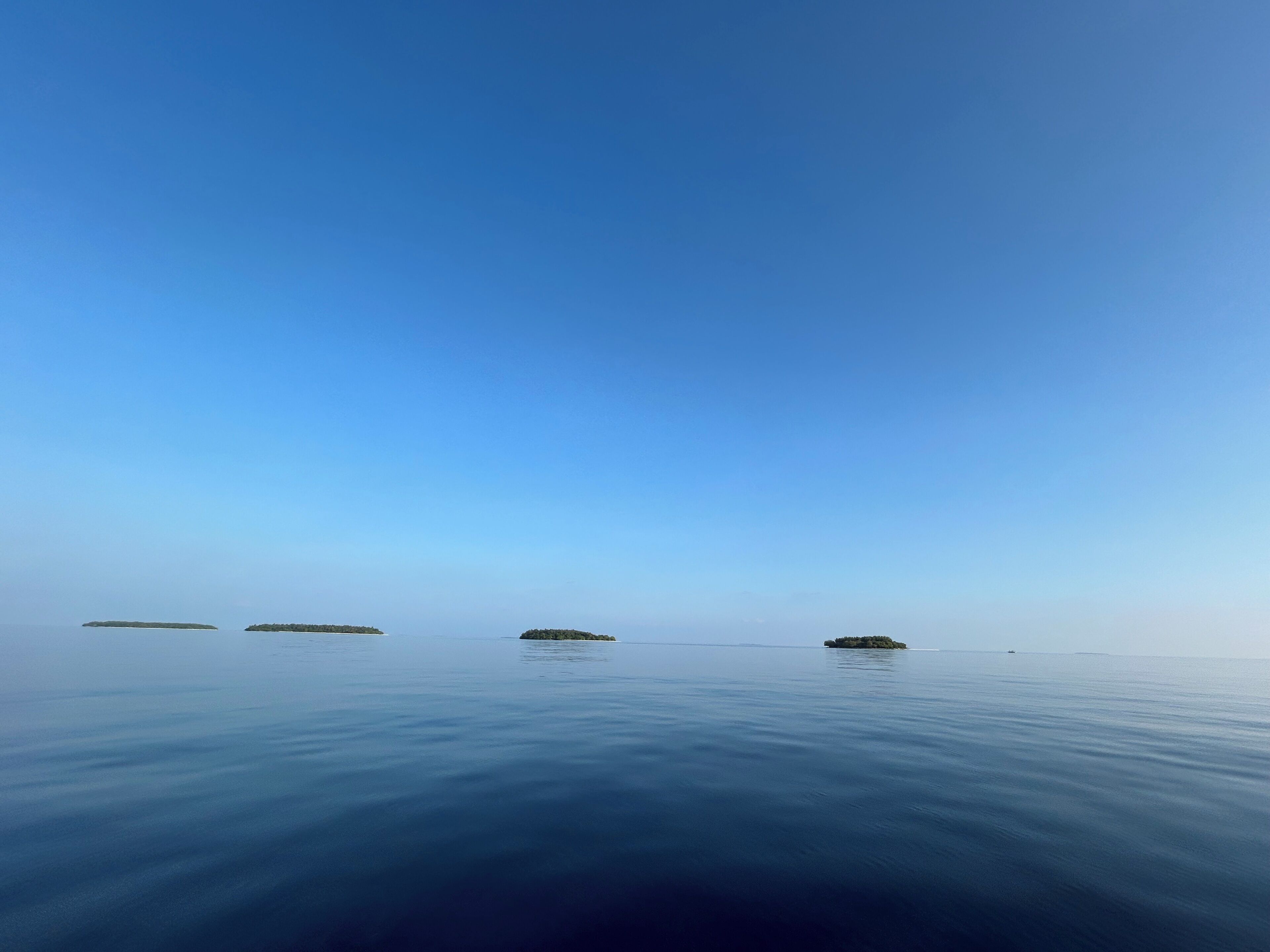 Mar tranquila con tres islas pequeñas a lo lejos bajo un cielo despejado.