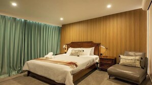 A hotel room with a large bed, a wooden headboard, a nightstand, a chair, and a wooden wall panel. - Alpine Studio Coulson (Lake Tekapo)