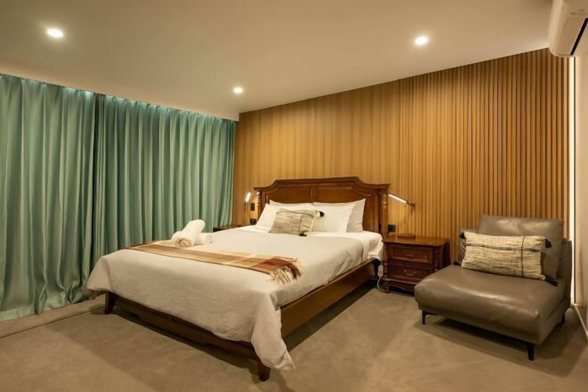 Une chambre d’hôtel avec un grand lit, une tête de lit en bois, une table de chevet, une chaise et un mur avec des lambris en bois verticaux.