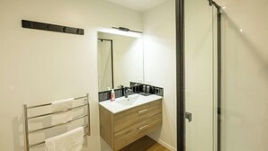 A modern bathroom with a wooden vanity, a towel rack, and a glass shower enclosure. - Alpine Studio Coulson (Lake Tekapo)