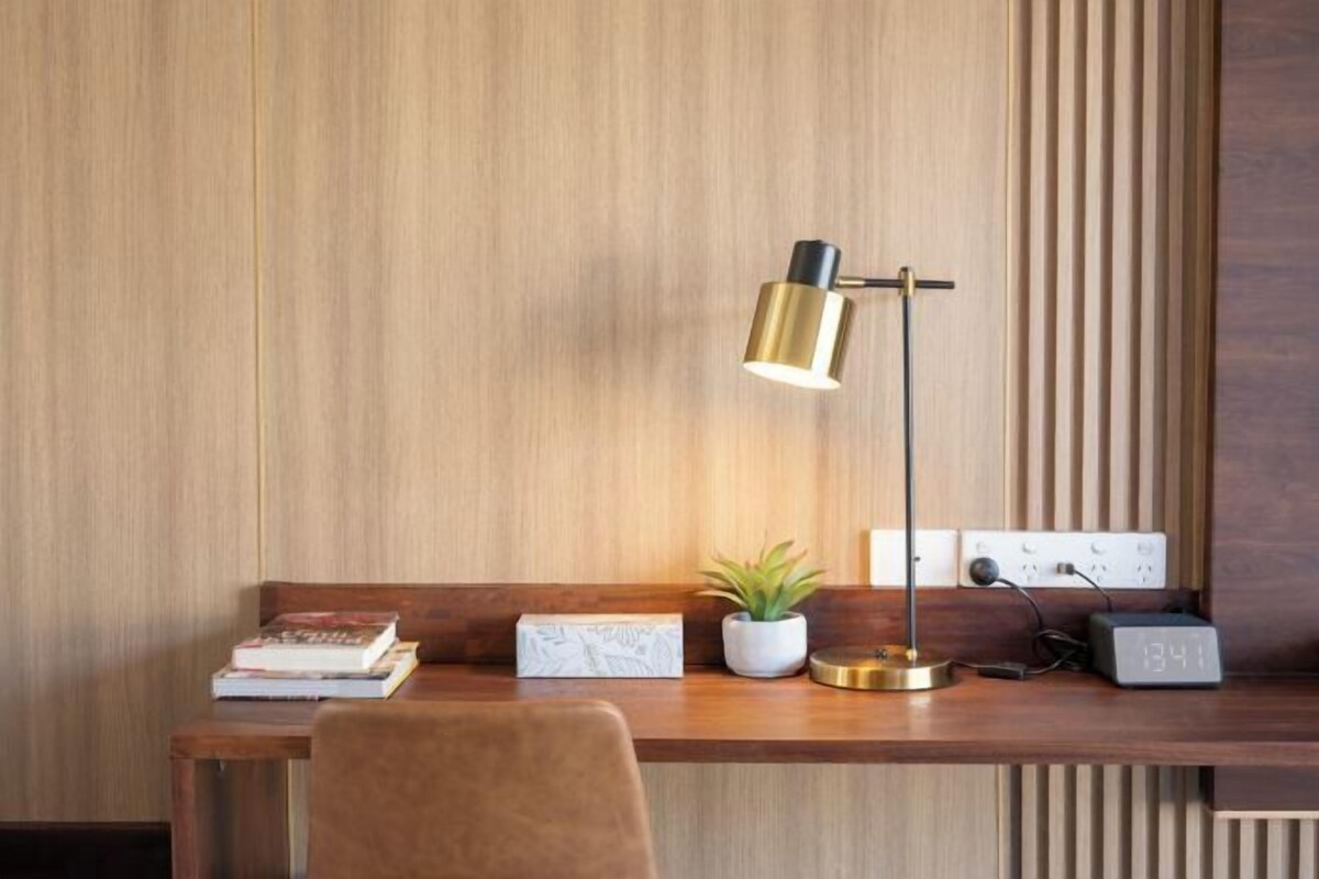 A wooden desk with a lamp, a potted plant, a clock, and books.
