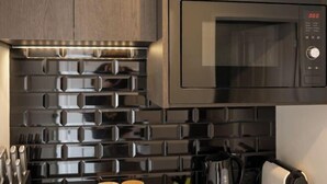 A modern kitchen with a stainless steel microwave, a brick-patterned backsplash, and a set of knives on the counter. - Alpine Studio Coulson (Lake Tekapo)