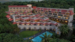 Un hotel de varios pisos con techo rojo, múltiples balcones y una piscina rodeada de vegetación.