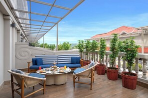 A rooftop terrace with a blue-striped sofa, wicker chairs, a round table with food, and potted plants. - Grand Mercure Goa Candolim (Marra)