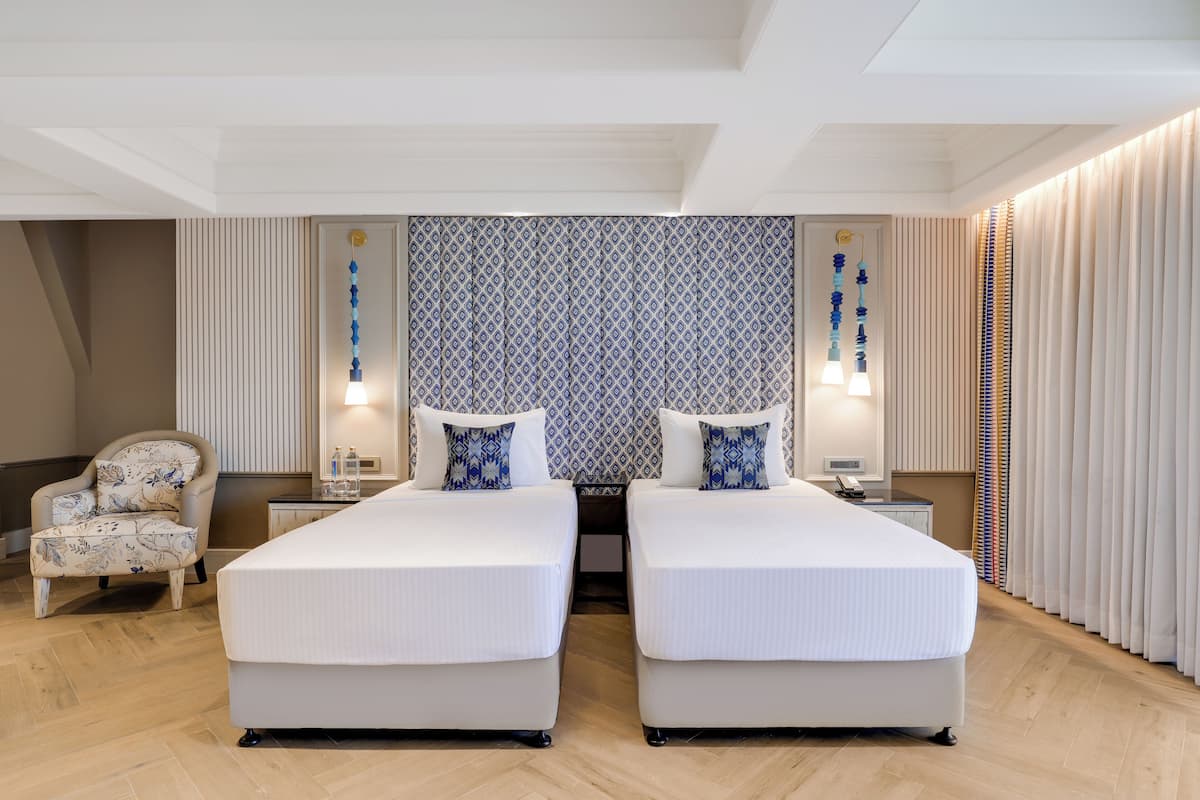 A hotel room with two beds, a chair, bedside tables, and a patterned wall.