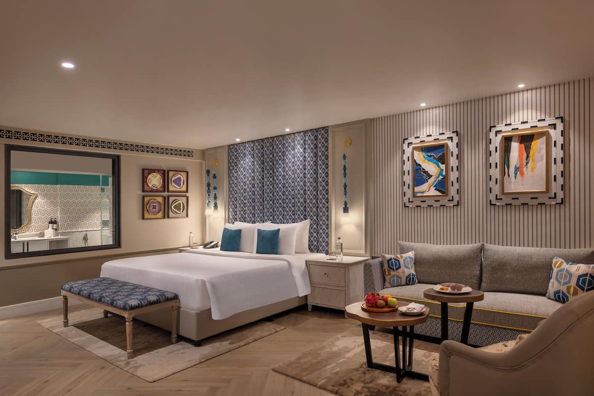A modern bedroom with a large bed, bedside tables, a bench, a sofa, and artwork on the walls.