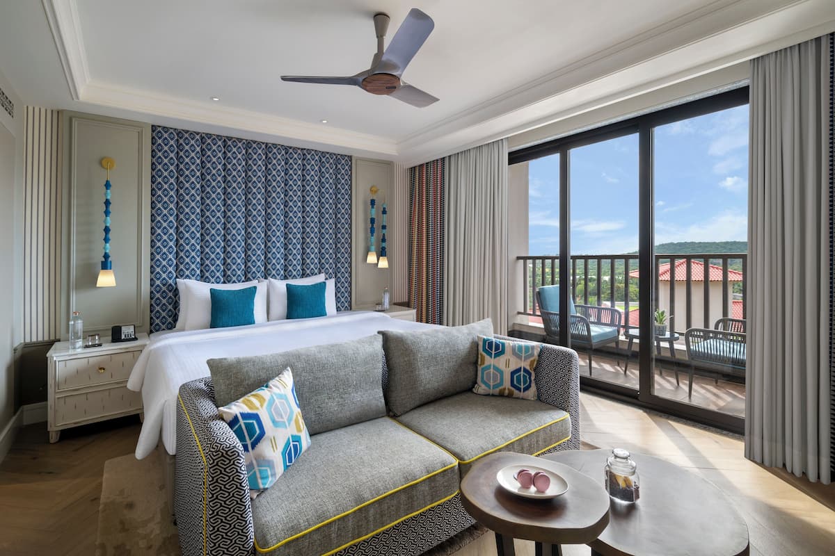 A hotel room with a large bed, a sofa, a small table, and a balcony with a view.